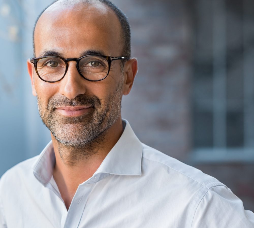 Portrait of happy mature man wearing spectacles and looking at camera outdoor. Man with beard and glasses feeling confident. Close up face of hispanic business man smiling.